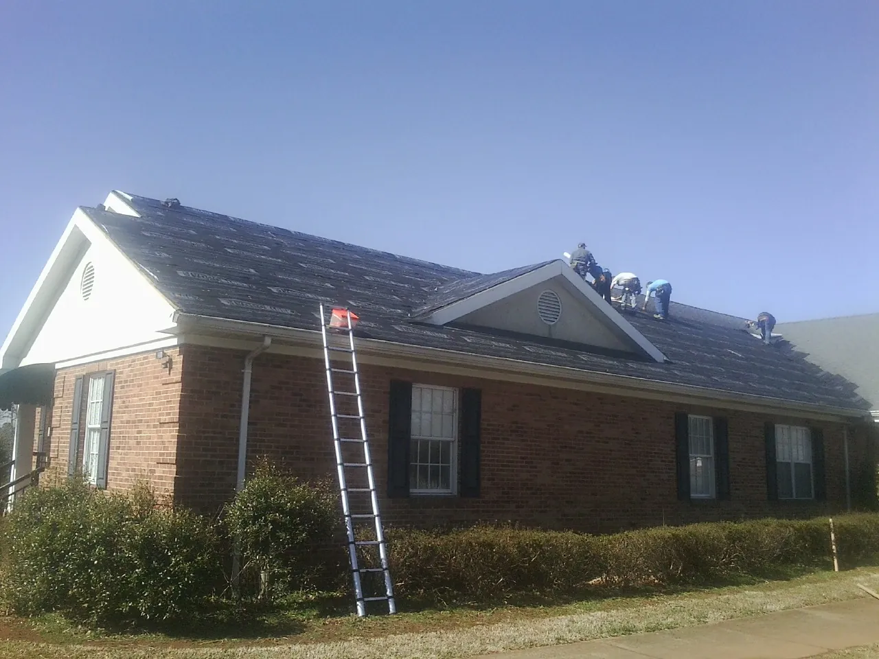 Crew tearing shingles off a brick ranch roof with a ladder set — Metal Roof Repair work by our crew in Glenarm
