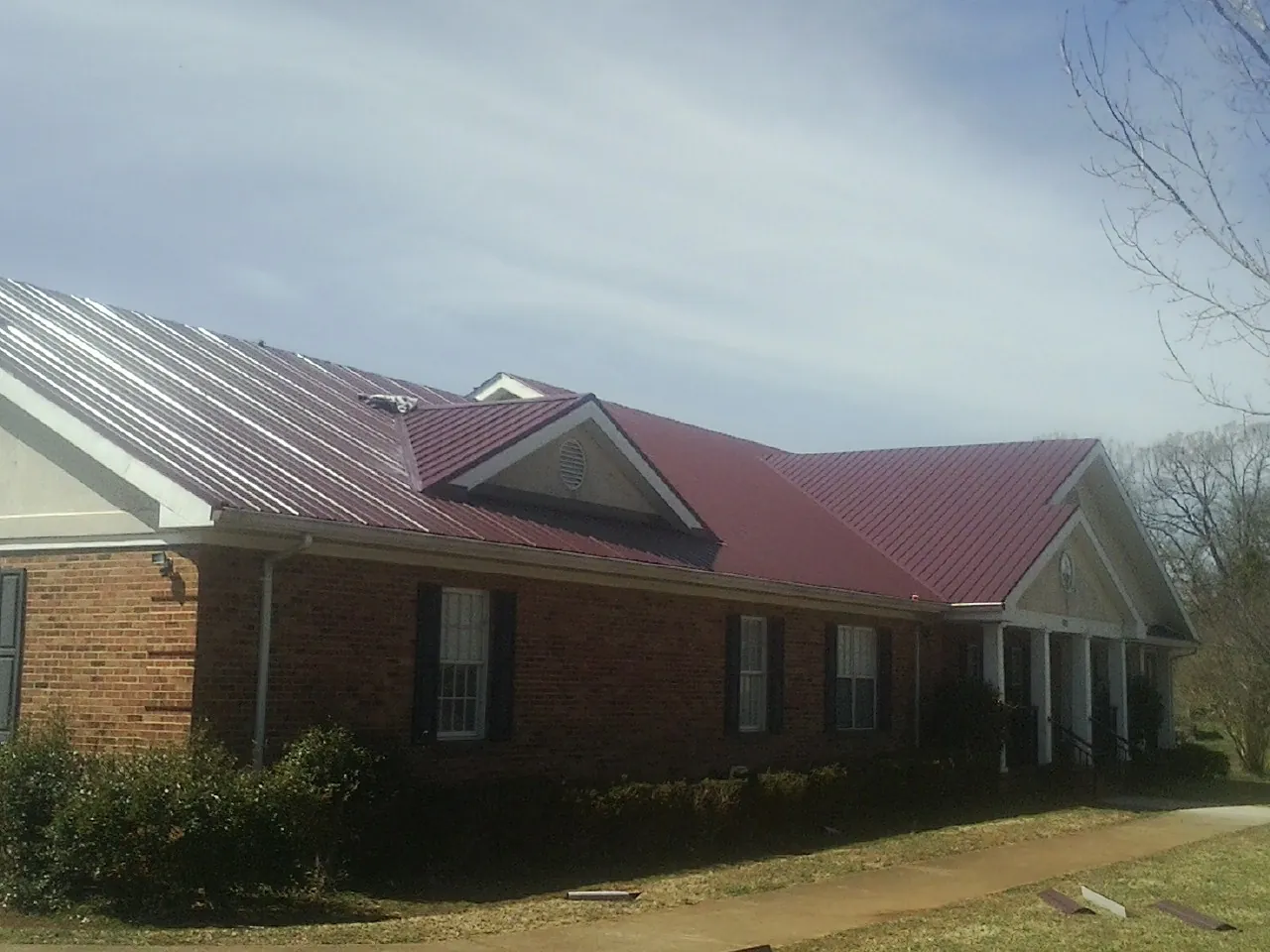 Red metal roof with gabled entries on a long brick building, from a Hail Damage Roof Repair job in Glenarm