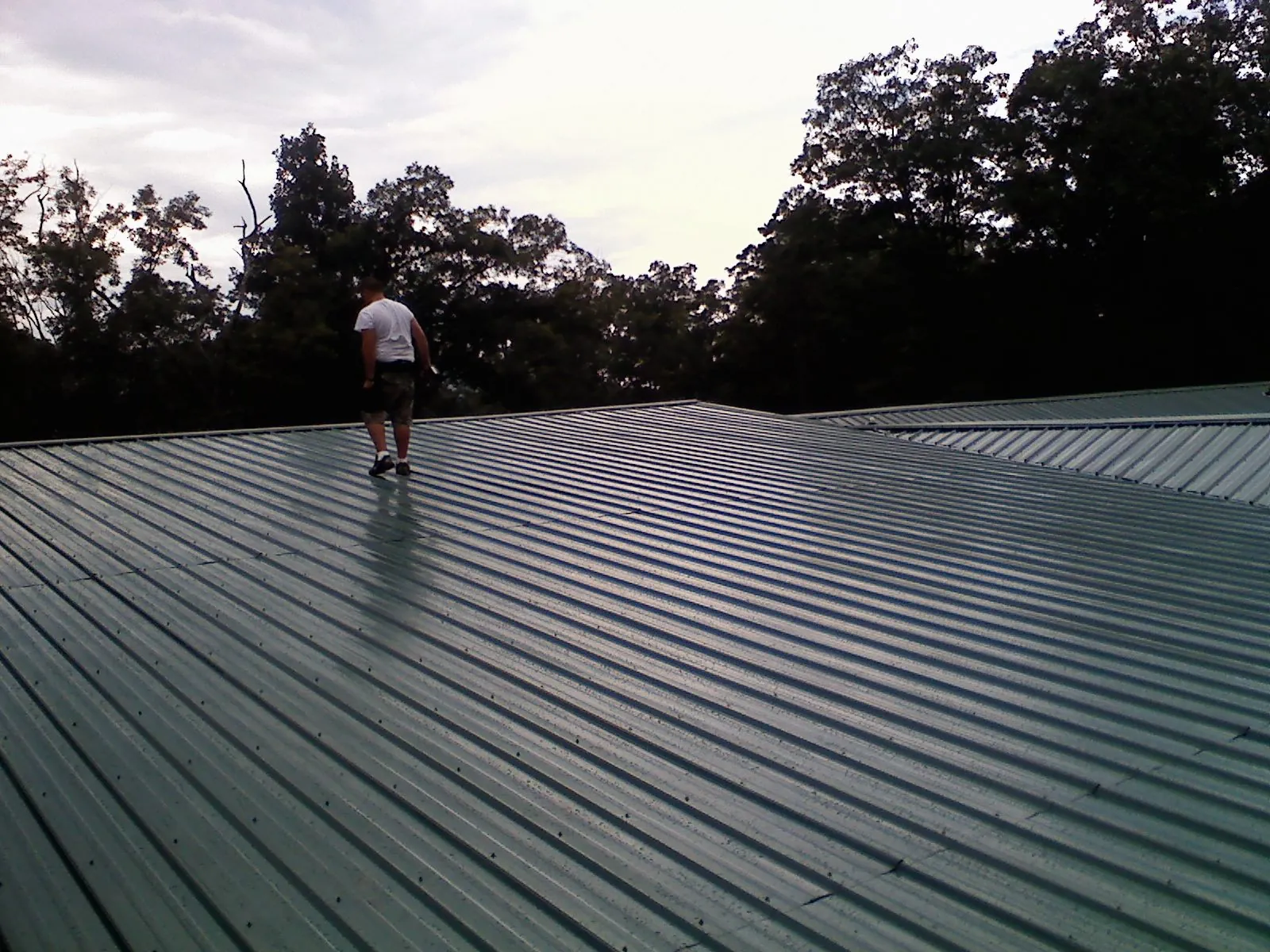 Roofer walking a wide expanse of new green metal roofing in Glenarm