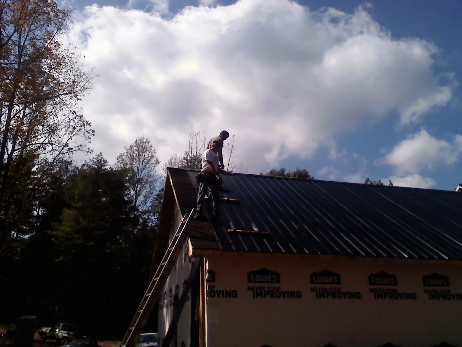 Roofer fastening dark metal panels high against a cloudy sky, from a Roof Inspection job in Glenarm