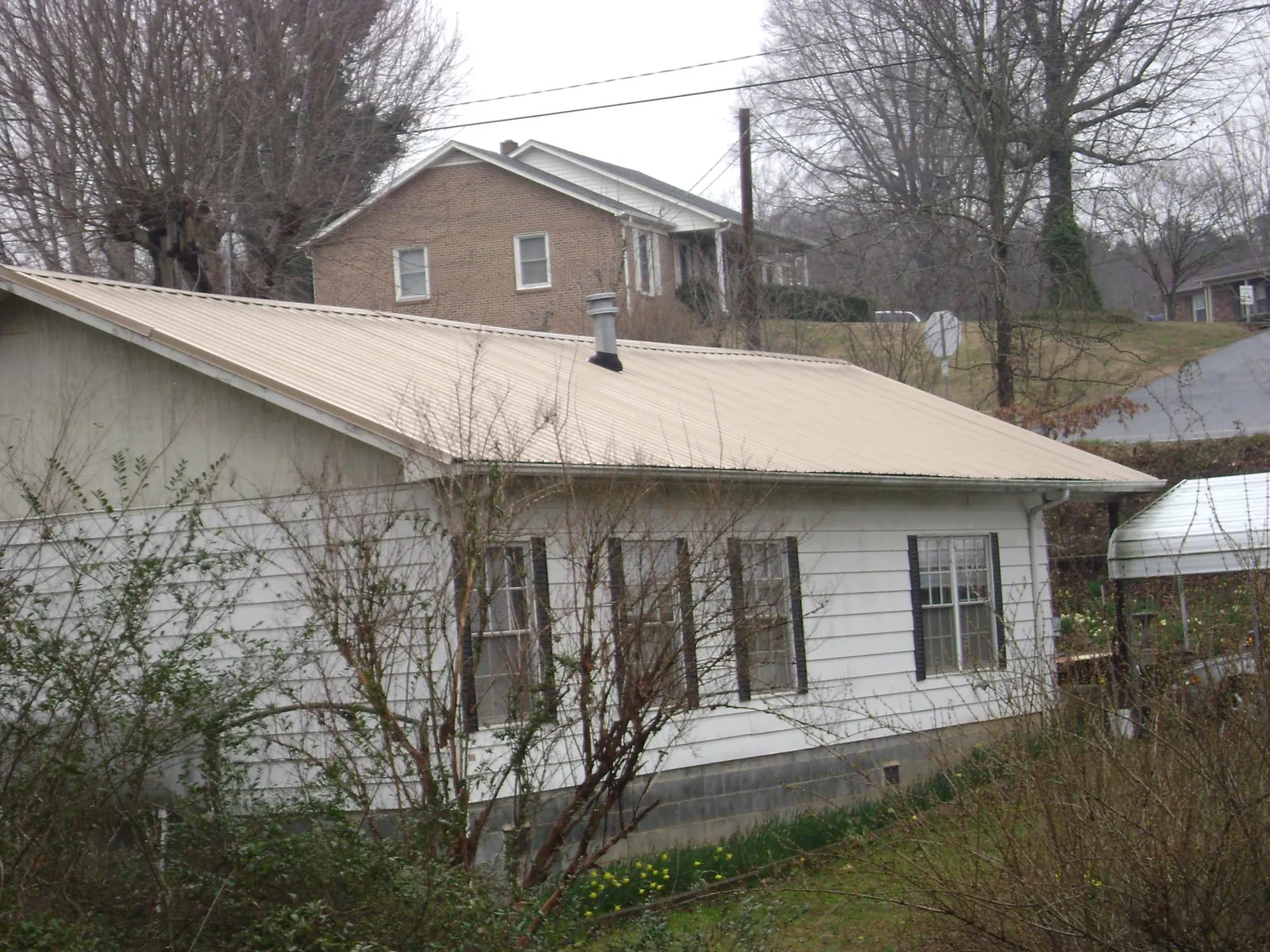 Tan metal roof on a white sided house set into a hillside — Commercial Roofing by Roofing Brothers in Glenarm