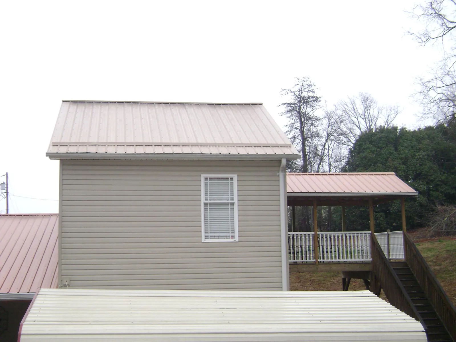 Tan metal roofs on a two story addition and attached porch, from a Roof Replacement job in Glenarm